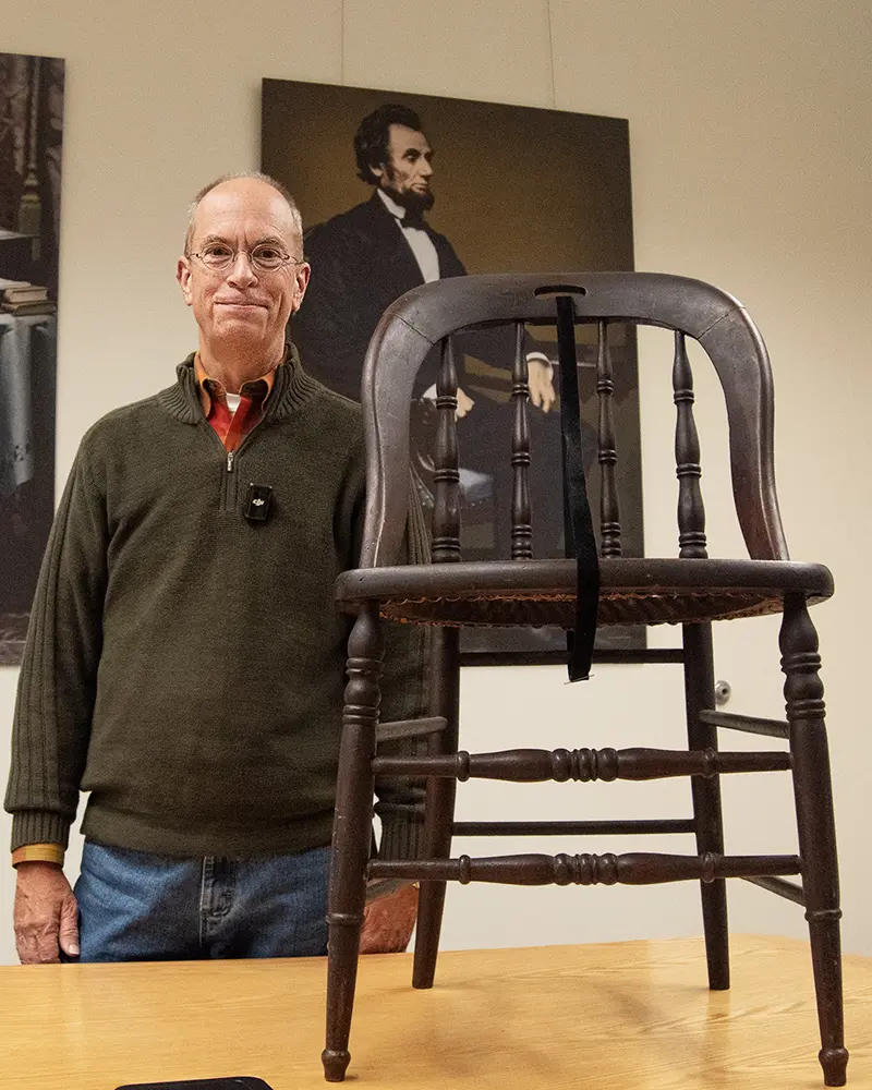 Photo of Gordon McCray standing beside a chair he has donated to the ALPLM.