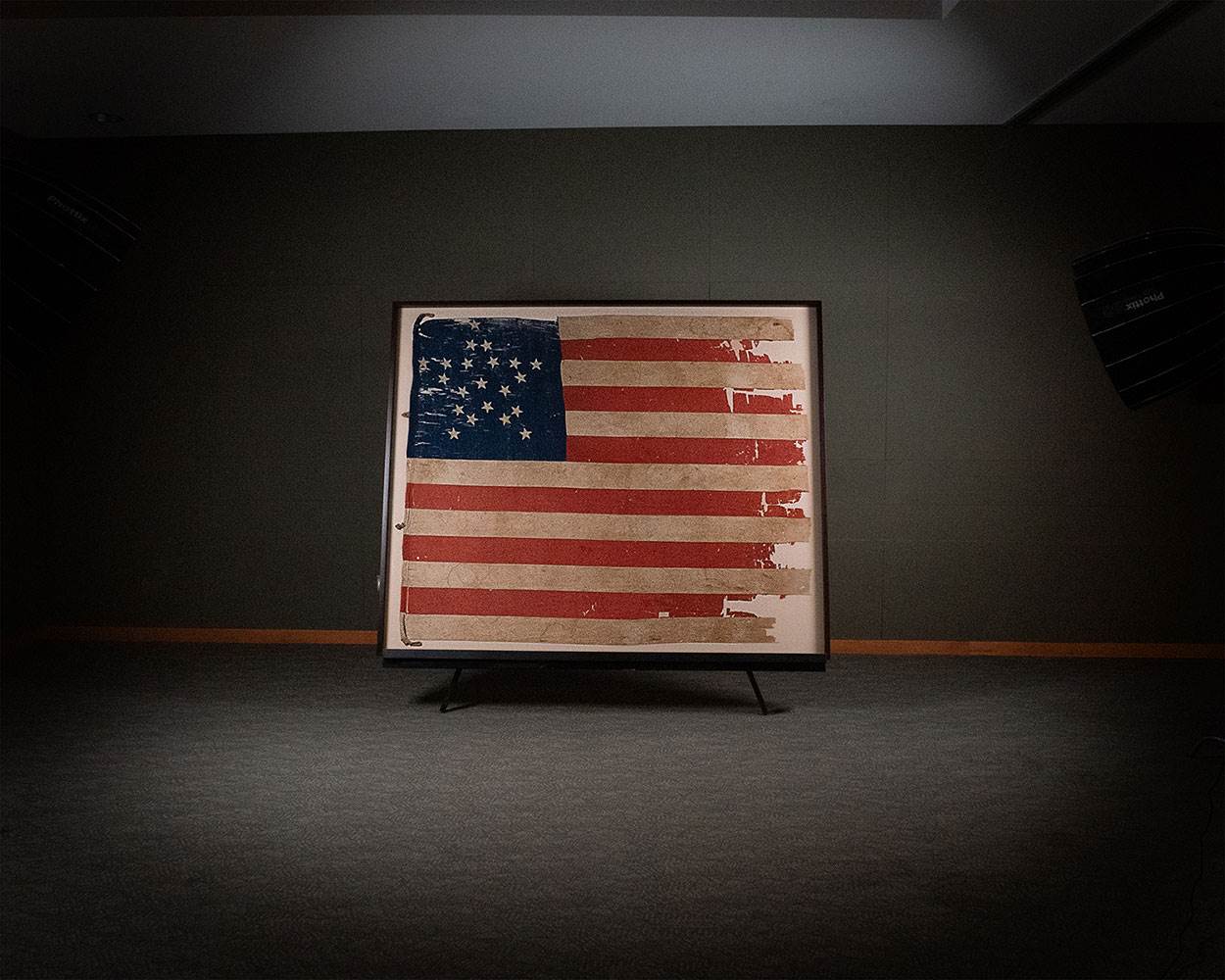 Photo of a large, tattered flag with 21 stars arranged in a star pattern.