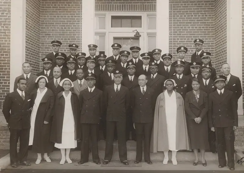 A group of African American men and women posing in rows outside a brick building.